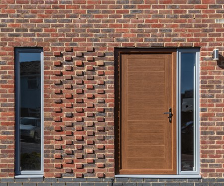 Red brick wall with alternate brick ends protruding. A solid front door and two tall windows.